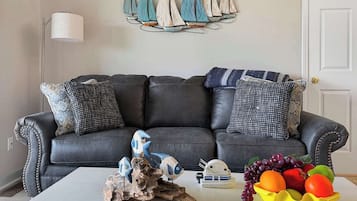 Een woonkamer met een donker leren bank, decoratieve wandkunst, een witte salontafel en een fruitschaal.