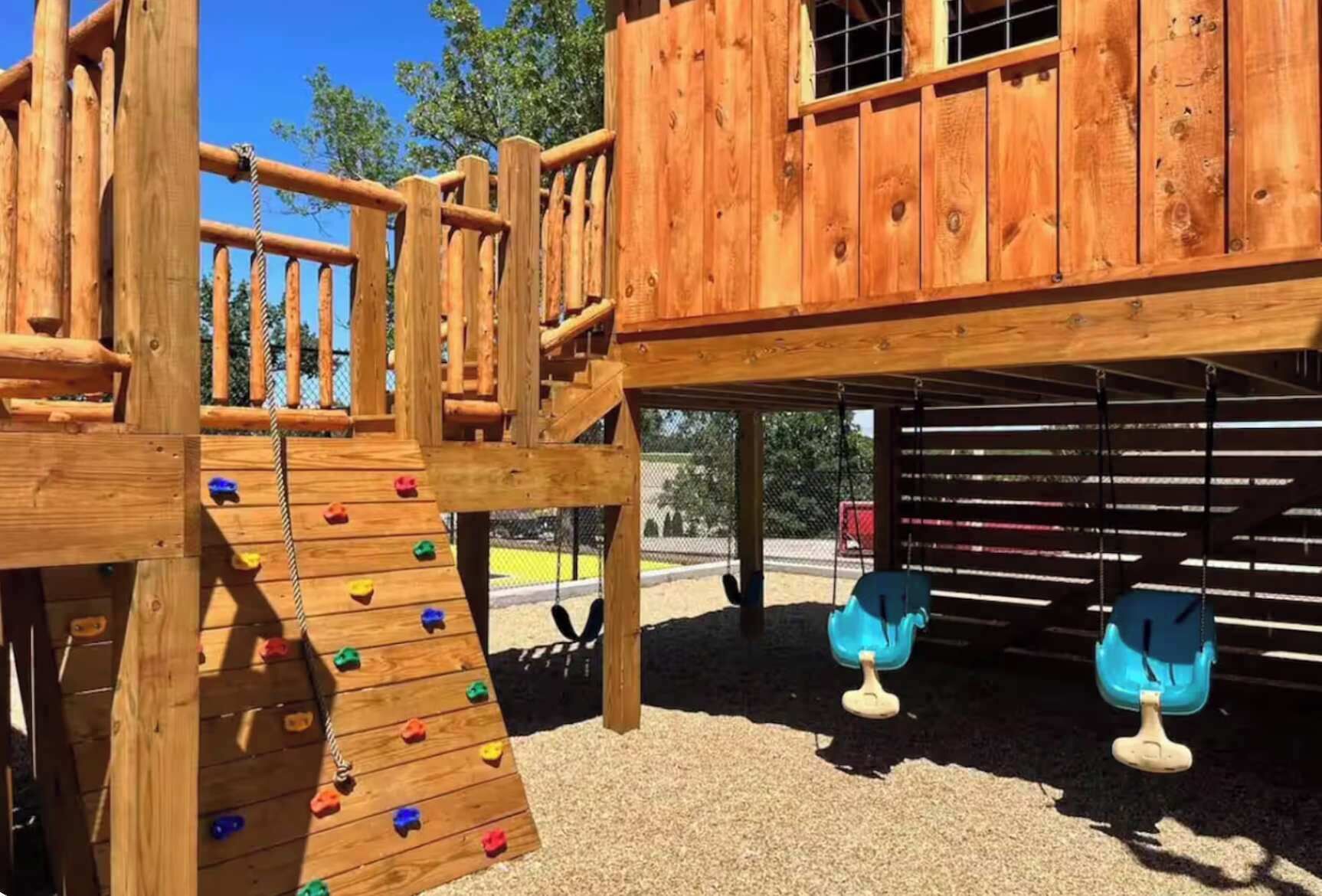 A wooden play structure with climbing elements and swings.