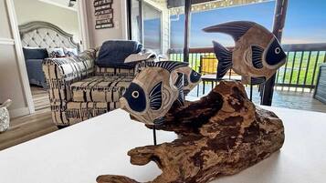 A room with a large window, a wooden table with fish sculptures, a patterned sofa, and a ceiling fan.