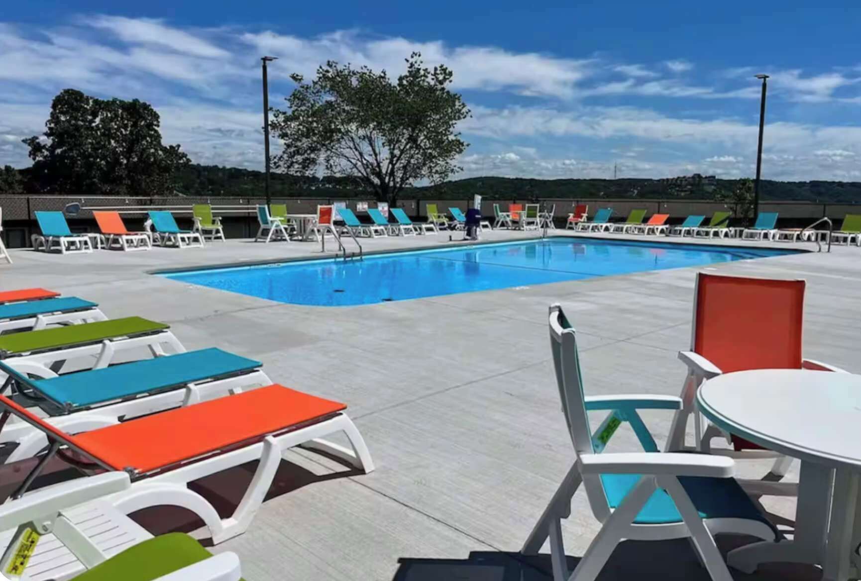 Una piscina con lettini e un tavolo, circondata da una recinzione e alberi.