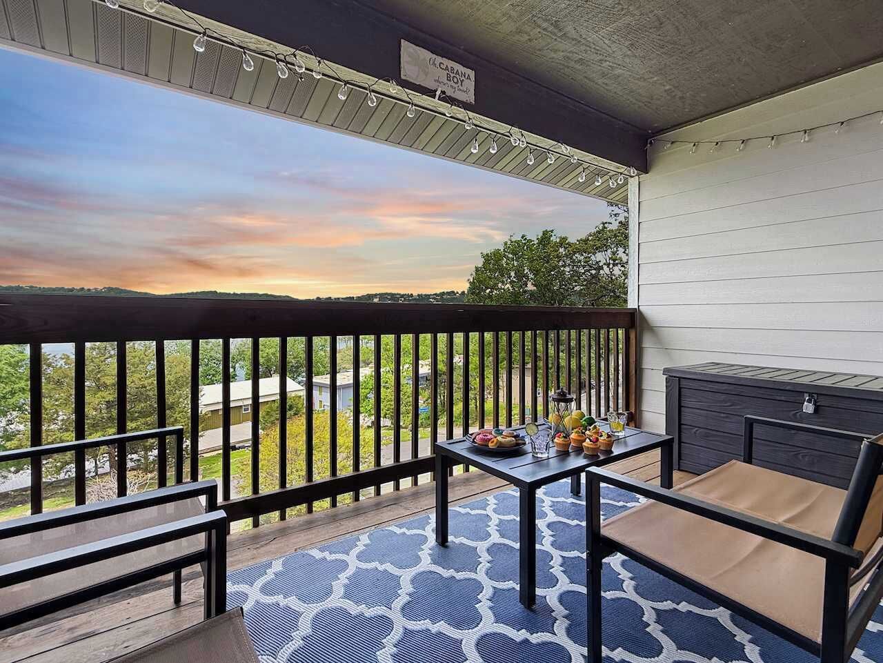 Een balkon met uitzicht op een zonsondergang, een tafel met eten en een zithoek.