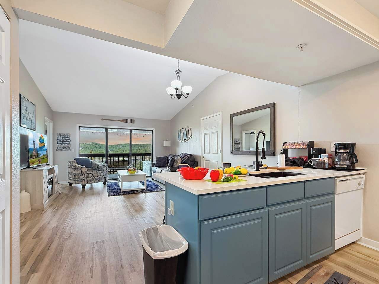 A modern kitchen with a large island, a dining area with a view, and a living room with a sofa and a TV.