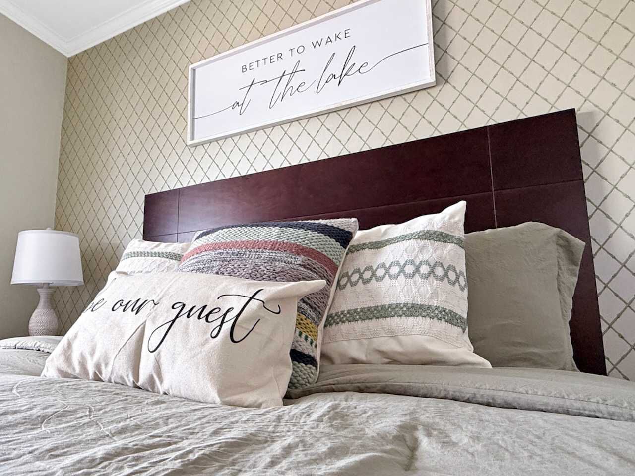 A neatly made bed with patterned pillows and a framed sign on the wall.