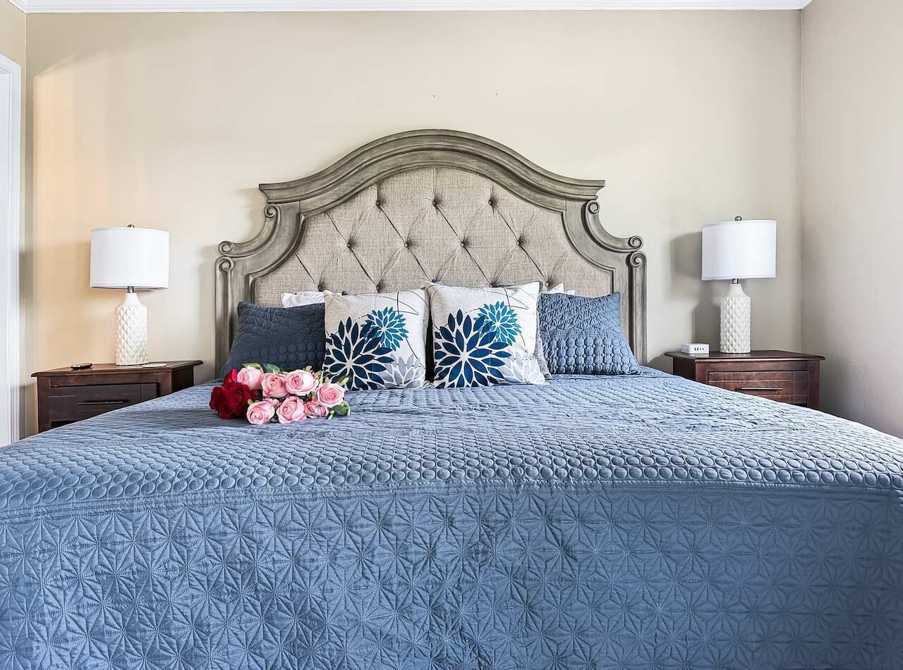 Un letto con testiera trapuntata, due comodini e un bouquet di fiori.