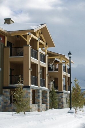 A multi-story building with balconies, stone base, and a snowy landscape. - Yellowstone | Adventure Base Retreat | Pool + Nature | 2BR (West Yellowstone)