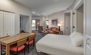 Une chambre d’hôtel comprenant un lit, une table à manger avec des chaises, un canapé, un fauteuil, une lampe et un ventilateur de plafond.