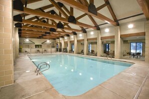 Une piscine intérieure dotée d’un sol carrelé, de poutres en bois et d’espaces aménagés pour s’asseoir.