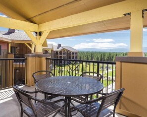 Une terrasse extérieure couverte, dotée d’une table ronde et de chaises, qui offre une vue sur une zone boisée.