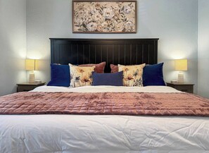 A hotel room with a large bed, two bedside tables with lamps, a dark headboard, and a floral painting above the bed. - No Stairs, Lakeside, beautiful patio and yard (Branson)