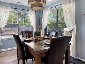 A dining area with a marble table, leather chairs, a woven light fixture, and a view of the outdoors through large windows. - No Stairs, Lakeside, beautiful patio and yard (Branson)