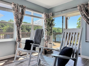 A room with a rocking chair, a potted plant, and a view of a wooden deck and trees. - No Stairs, Lakeside, beautiful patio and yard (Branson)