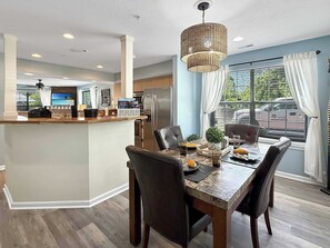 A modern kitchen with a central island, dining area with dark chairs, and a large window with curtains. - No Stairs, Lakeside, beautiful patio and yard (Branson)