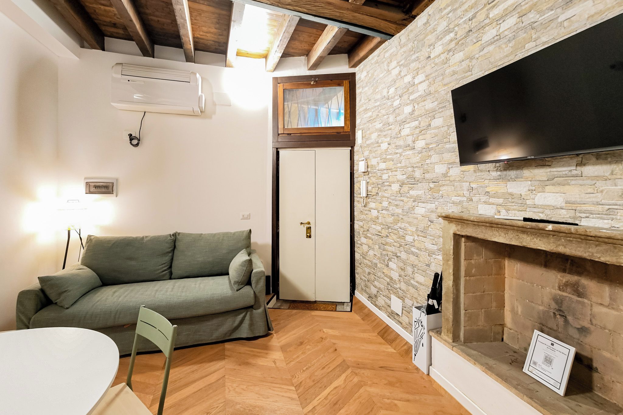 A cozy living room with a stone wall, a fireplace, a television, a sofa, and a door.