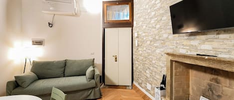 A cozy living room with a stone wall, a fireplace, a television, a sofa, and a door.
