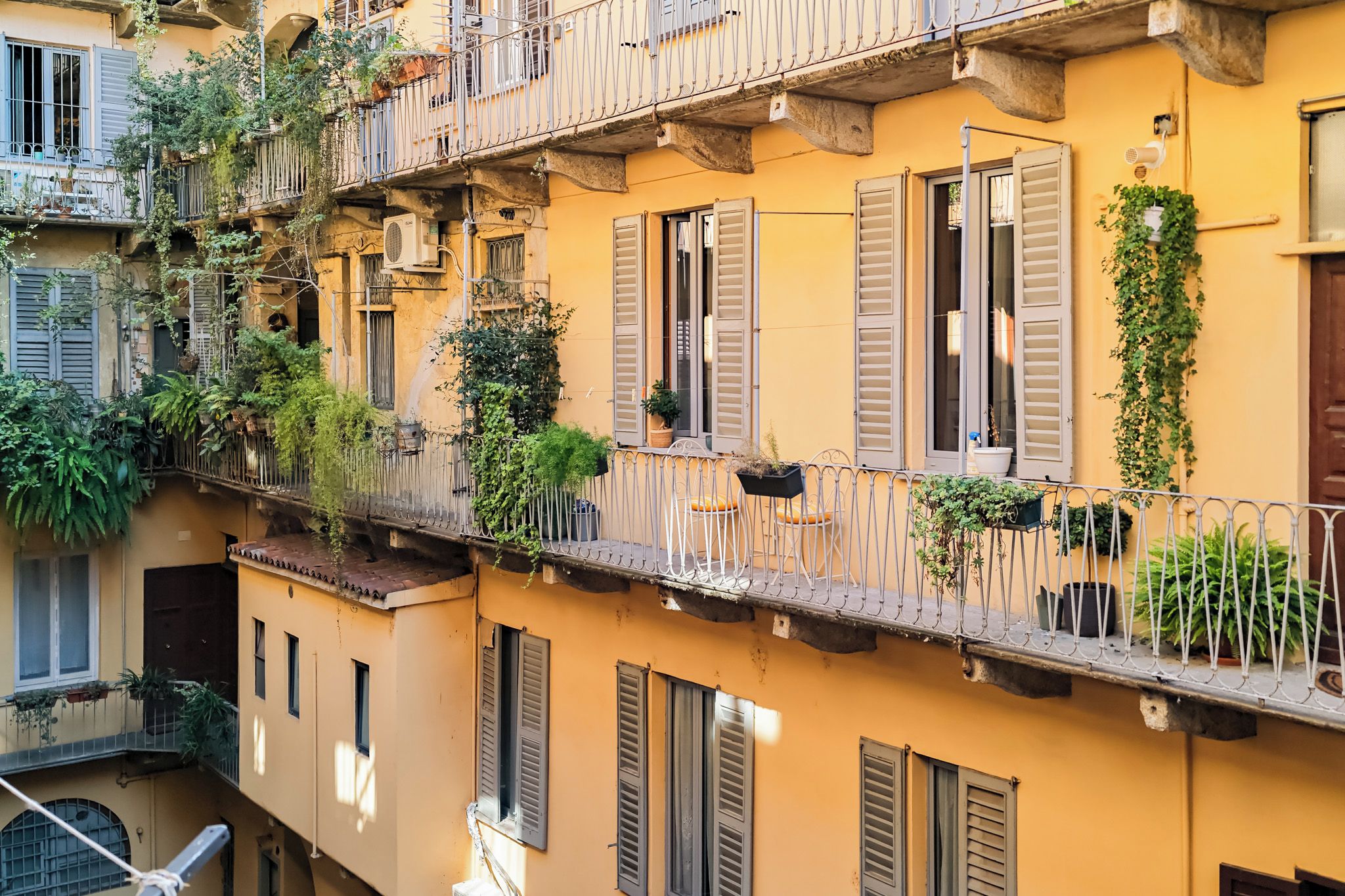 Un immeuble à plusieurs étages doté de balcons, dont certains sont ornés de plantes et de mobilier d’extérieur.