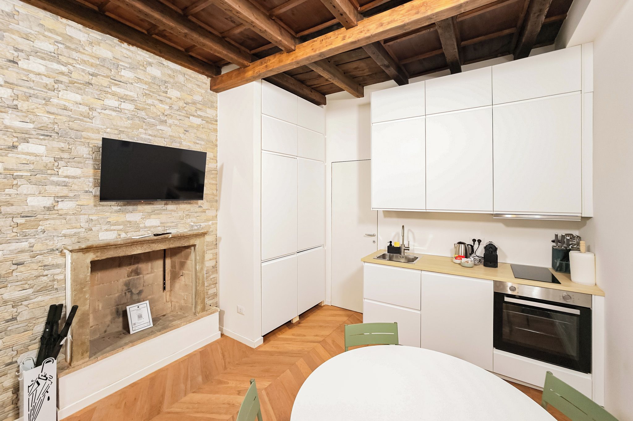 A modern kitchen with white cabinets, a built-in oven, a microwave, and a stone wall.