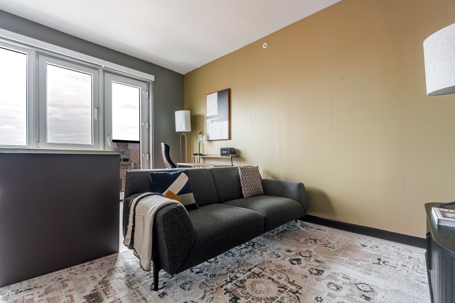A modern living room with a grey sofa, patterned rug, and a large window providing natural light.