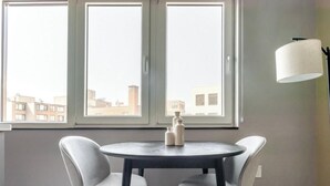 A room with a round table and two chairs, a window with a view of buildings, and a floor lamp. - Blueground | Downtown, gym, nr National Mall (Washington, D.C.)