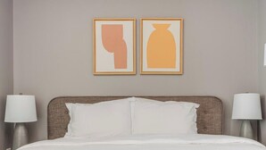 A hotel room with a bed, two bedside lamps, and two framed abstract art pieces on the wall. - Blueground | Downtown, gym, nr National Mall (Washington, D.C.)