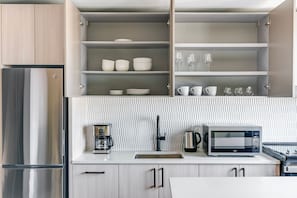 A modern kitchen with a built-in microwave, coffee maker, and kettle on the countertop. - Blueground | Downtown, gym, nr National Mall (Washington, D.C.)