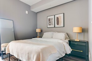 A bedroom with a bed, two bedside tables, a nightstand, a mirror, and two wall-mounted picture frames. - Blueground | Downtown, gym, nr National Mall (Washington, D.C.)