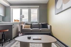 A modern living room with a grey sofa, a round coffee table, and a bar stool. - Blueground | Downtown, gym, nr National Mall (Washington, D.C.)