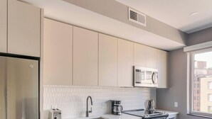 A modern kitchen with a built-in microwave, a stainless steel refrigerator, and a window providing a view of the cityscape. - Blueground | Downtown, gym, nr National Mall (Washington, D.C.)