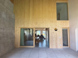 Un interior moderno con una pared de madera, un acceso por puerta de vidrio y un área de comedor con sillas y mesa.