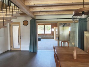 A spacious room with a wooden dining table, chairs, a clock on the wall, and a view through a large window. - Ferienwohnung Schof by Interhome (Tschierv)