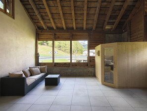 Una habitación con techo de madera, un sofá con cojines, suelo de baldosas y una sauna.