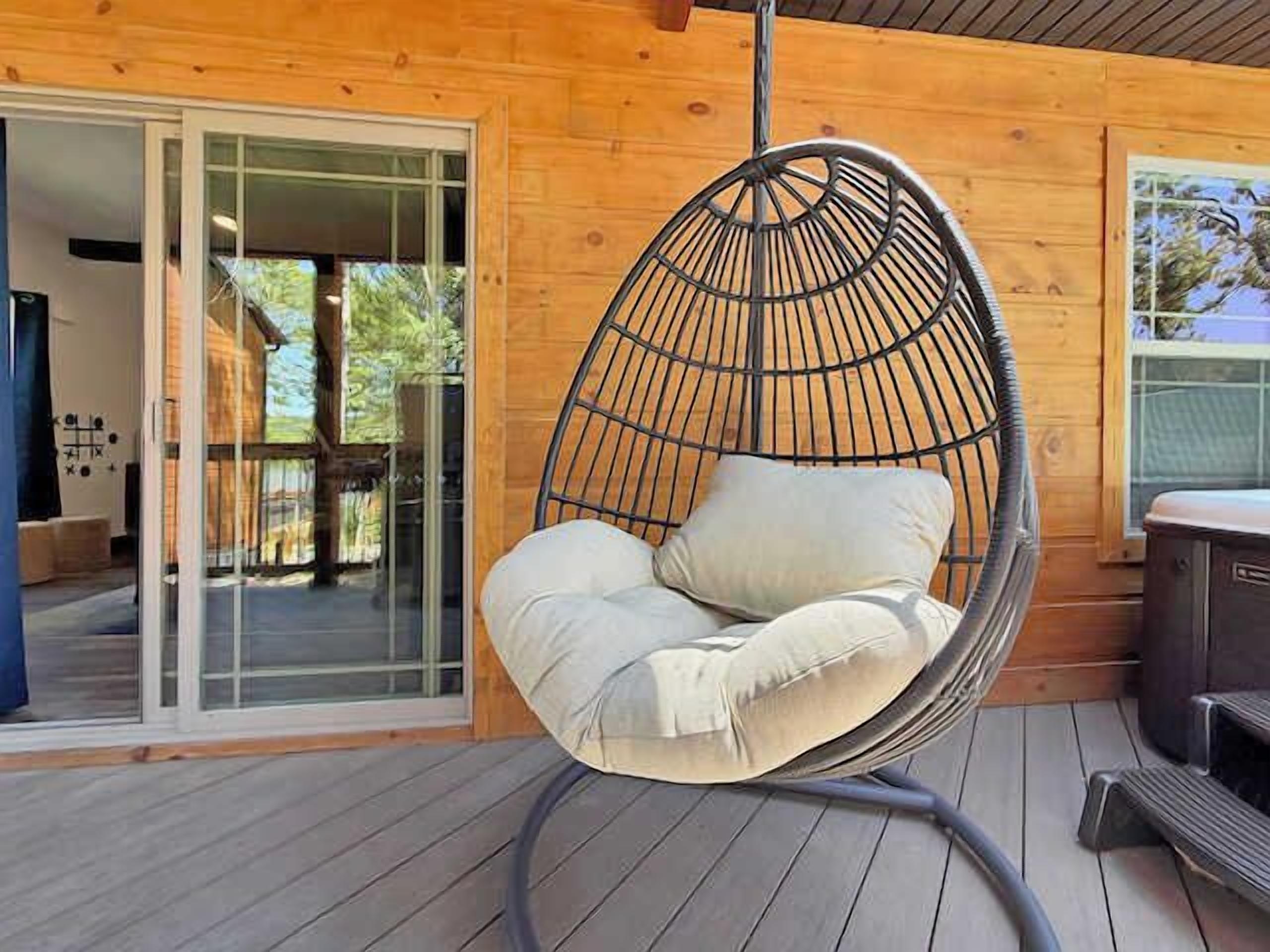 Un fauteuil suspendu avec des coussins, placé sur une terrasse en bois.