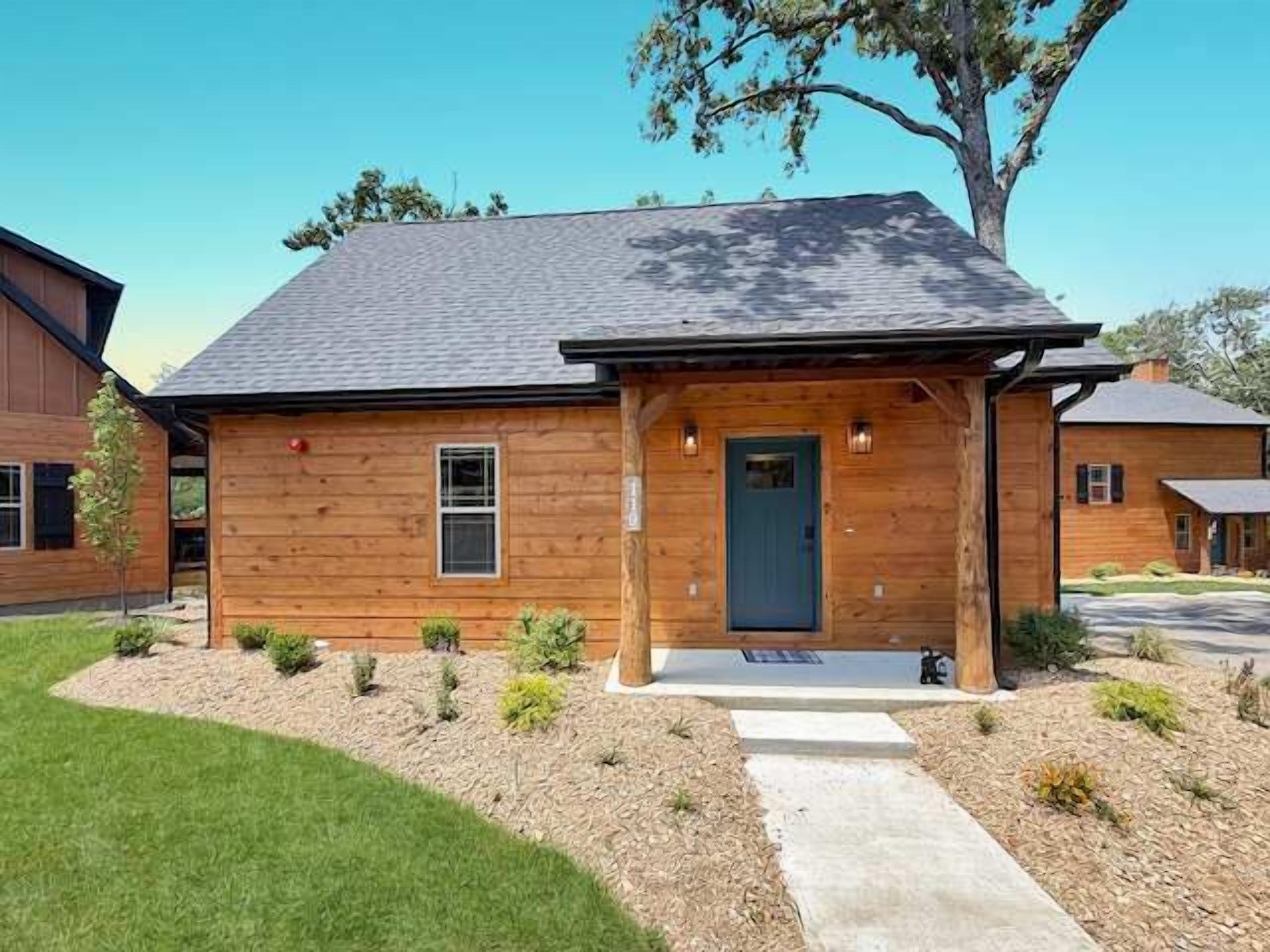 A wooden house with a dark roof, a front porch, and a small garden area.
