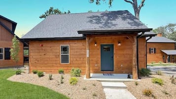 A wooden house with a dark roof, a front porch, and a small garden area.