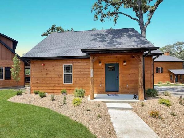 Una casa de madera con techo oscuro, un porche y un pequeño jardín.