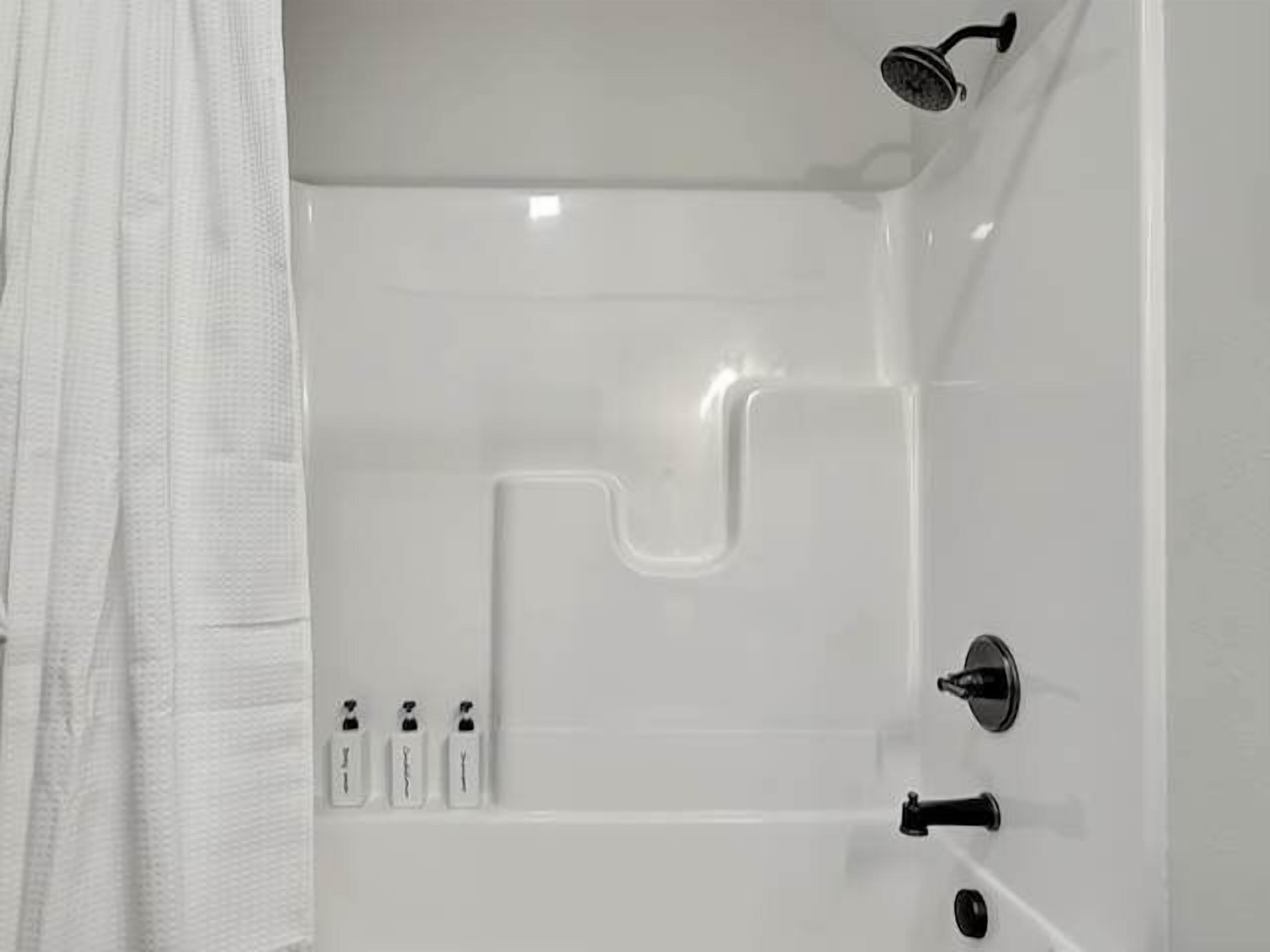 Une baignoire blanche avec un robinet, une pomme de douche et un bouton de commande.
