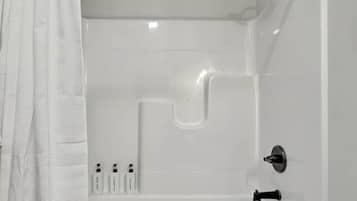 Une baignoire blanche avec un robinet, une pomme de douche et un bouton de commande.