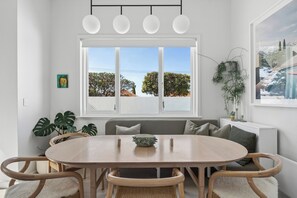A dining area with a round table, chairs, a bench, and a window with a view of trees and buildings.