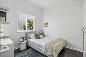 A bedroom with a bed, bedside table, and a window with a view of greenery.