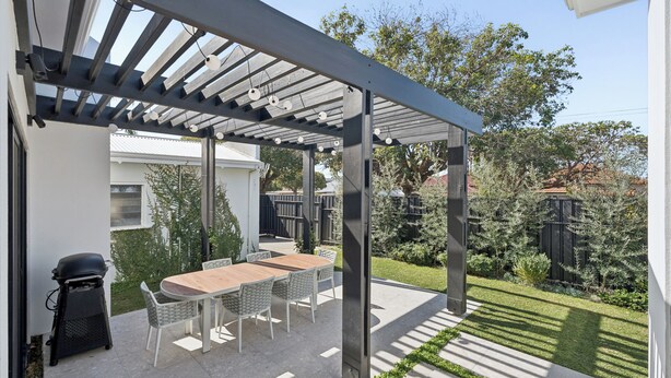 Un portico coperto con tavolo e sedie, un barbecue e un giardino.