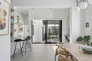 A modern kitchen with a white countertop, black bar stools, and a dining area with a wooden table and chairs.