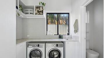 A laundry room with two front-loading washers, a tiled backsplash, a window with a view, and a white toilet.