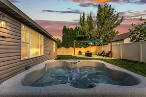 A backyard with a hot tub, a covered patio area, and a wooden fence.