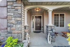 A house entrance with a stone facade, a welcome sign, and a porch with a table and chairs.