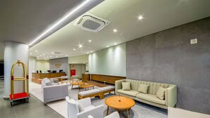 A hotel lobby with a reception desk, seating area with sofas and chairs, and a luggage cart.