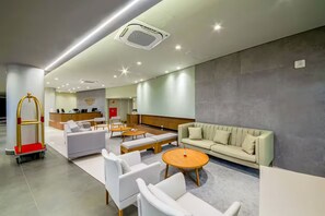 A hotel lobby with a reception desk, seating area with sofas and chairs, and a luggage cart.