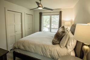 A bedroom with a bed, a ceiling fan, a window with curtains, and a bedside lamp. - Wapo Retreat (Amery)