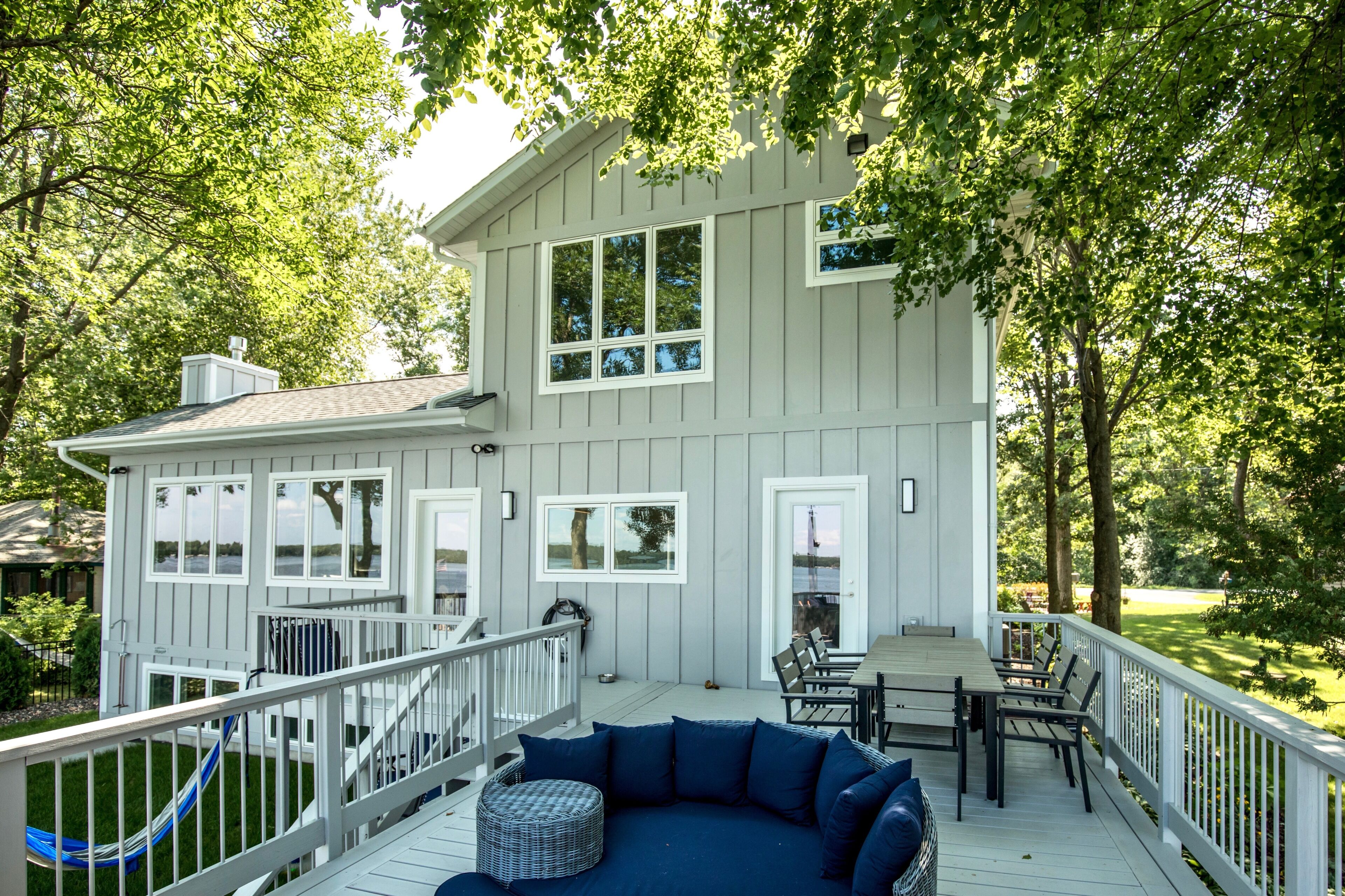 A two-story house with a deck, outdoor seating, and a view of the water.