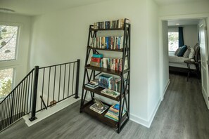 A multi-tiered bookshelf in a hallway with a staircase on the left. - Wapo Retreat (Amery)