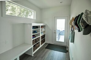 A hallway with a white storage unit, a door with a view to the outside, and a wall with hats hanging. - Wapo Retreat (Amery)