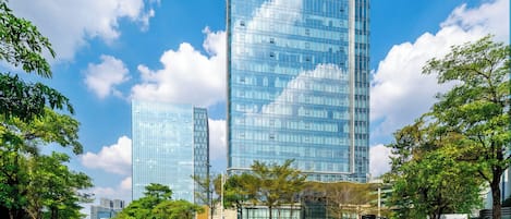 A modern urban street with two high-rise buildings, one with a visible sign, and a clear sky.